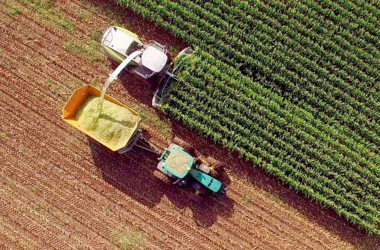 Aerial view of a combine harvester unloading grain beside a field